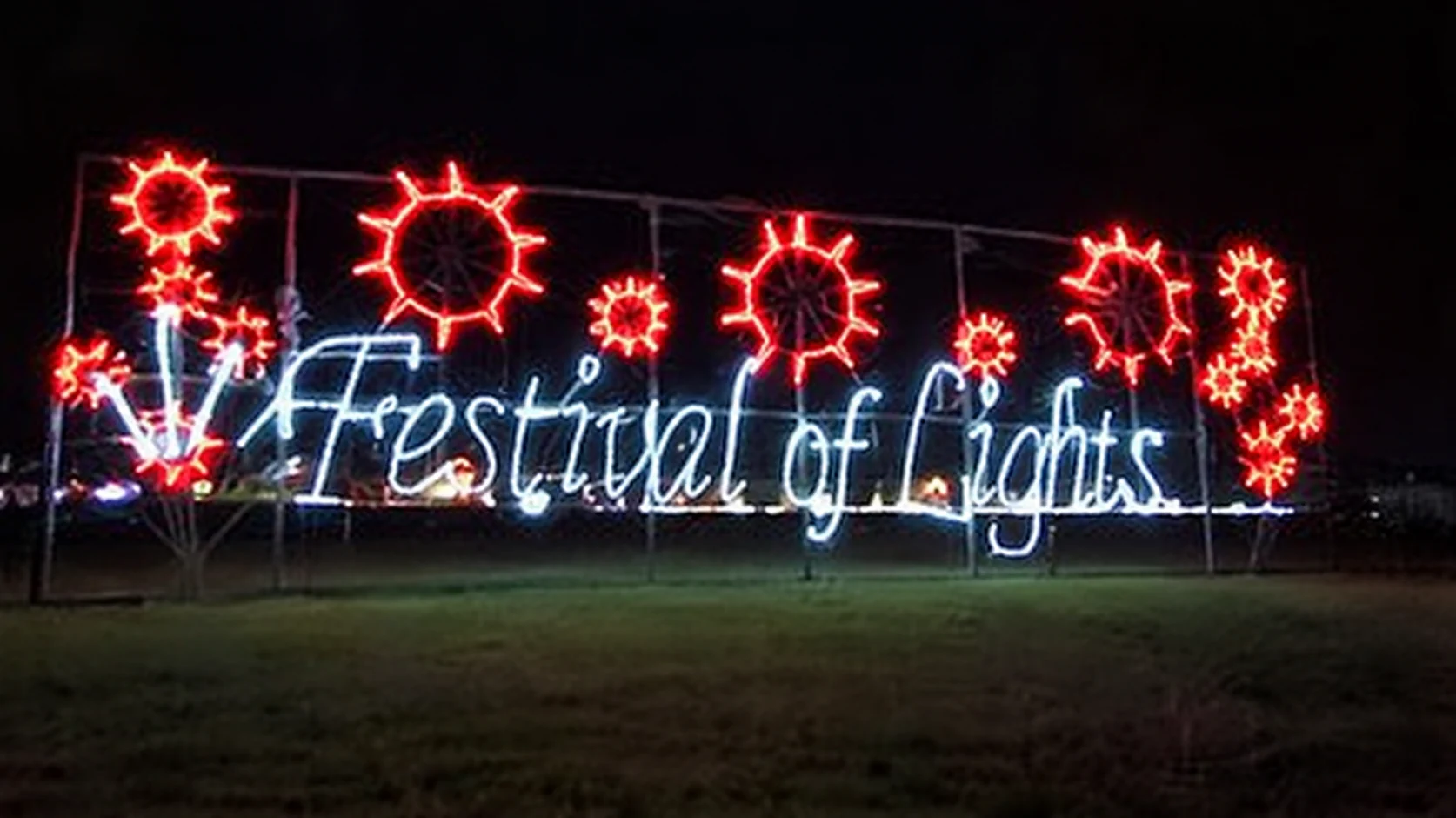 The Festival of Lights welcome sign glowing beneath red poinsettias.