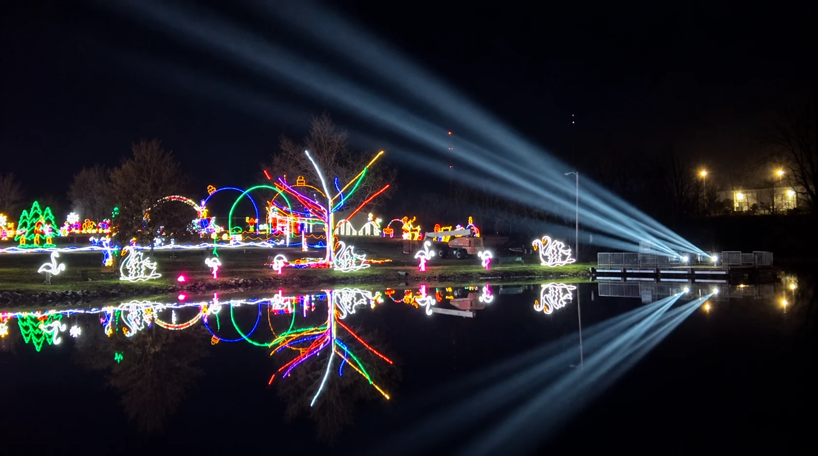 Christmas lights and sweeping white beams reflected across the park’s pond.